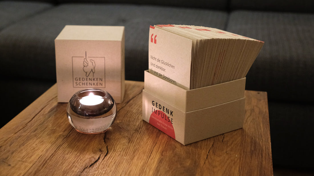 Trauergeschenk mit Gedenkimpulse-Karten und einer Kerze auf einem Holztisch.